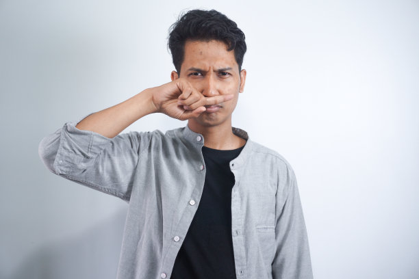 厌恶的人的肖像用手指捏鼻子，双手厌恶地看着有什么东西发臭难闻的情况孤立在灰色的墙壁背景。人的面部表情、肢体语言反应图片下载