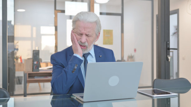 牙痛的资深商人在办公室用笔记本电脑工作图片下载