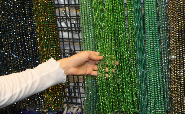 在购物中心的时尚饰品摊位上，女孩正在挑选一条绿色玻璃珍珠项链图片下载