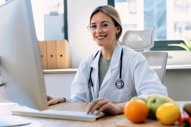 漂亮聪明的营养学家女人在营养学家咨询时看着相机，一边用电脑工作图片下载