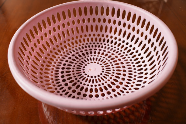 一个圆形的水果篮，上面有粉红色的洞，放在木桌上图片下载