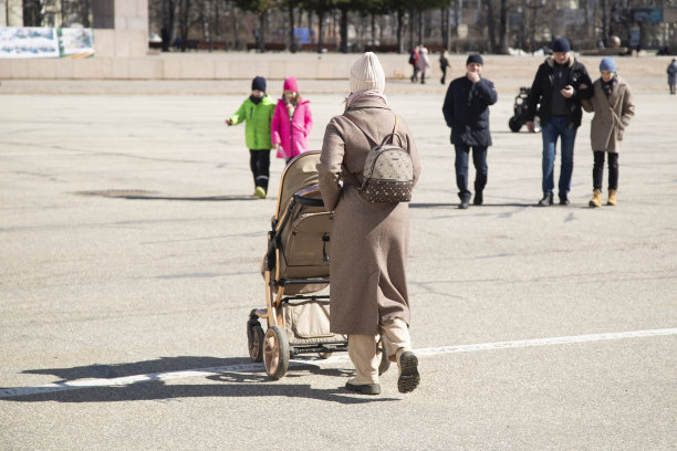 一名妇女推着婴儿车走着，车上有一个小孩。图片下载