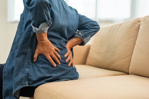 老老头的结构性姿势有问题他的背和脖子都痛。成熟的按摩他的背部缓解。减少肌肉紧张。坐在家里客厅的沙发上图片下载