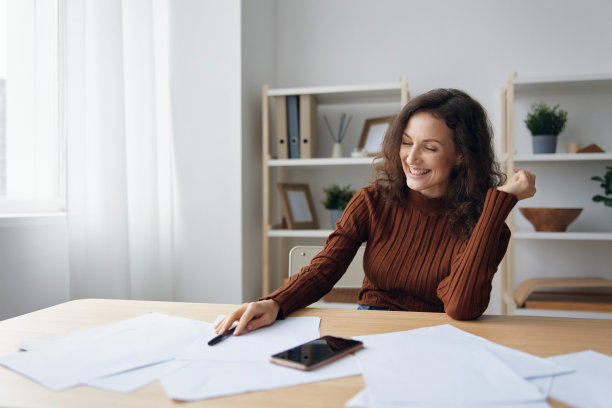 开朗快乐微笑的卷发女人写剧本计算税收计算采购预算看着桌子上电话旁边的文件。理财知识概念。抵押贷款优惠图片下载