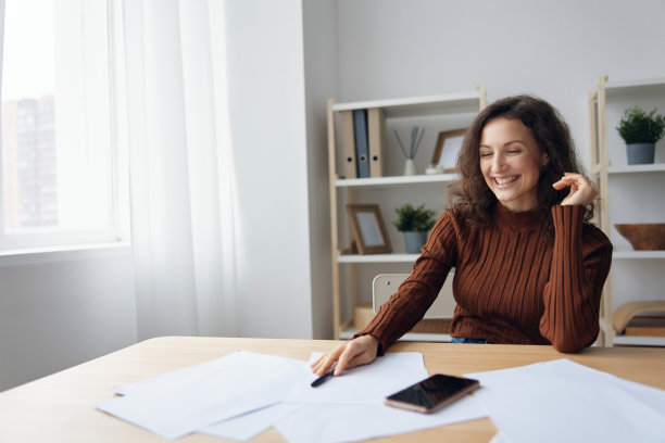 开朗快乐微笑的卷发女人写剧本计算税收计算采购预算看着桌子上电话旁边的文件。理财知识概念。抵押贷款优惠图片下载