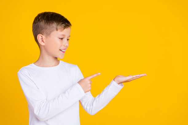 照片中非常积极的孩子穿着白衬衫微笑着，手指握着手臂，空白的空间孤立的黄色背景图片下载