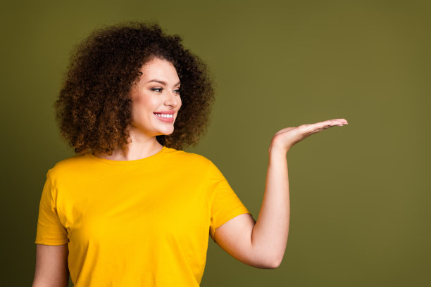 穿着黄色t恤的年轻快乐女士的照片展示了在卡其色背景上孤立的美容行业的新技术图片下载