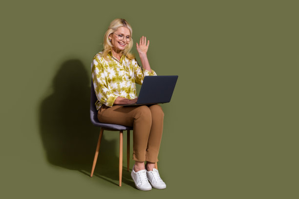 女老板坐在会议室的全长照片，在会议期间，在网上挥手打招呼，上网本在卡其色背景图片下载