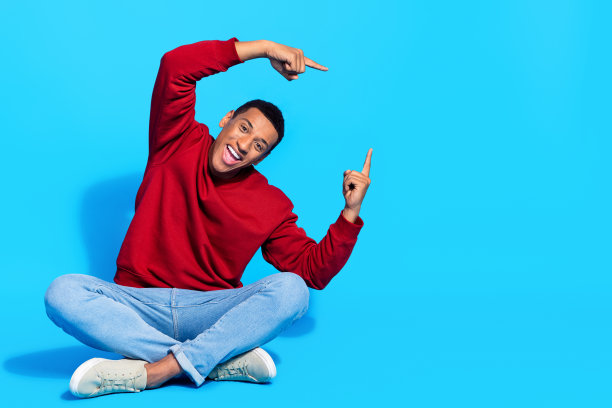 照片正面的好男人穿着时尚的红色衣服，两只手臂在头顶空的空间广告牌孤立的蓝色背景图片下载