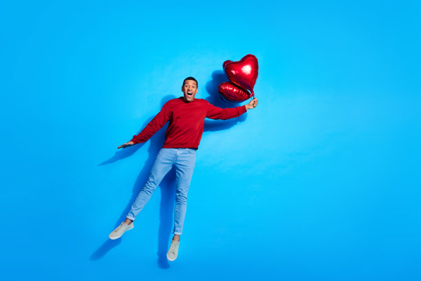 印象深刻的大喜过望的人的全长照片手臂抱心形气球跳飞空空间孤立的蓝色背景图片下载