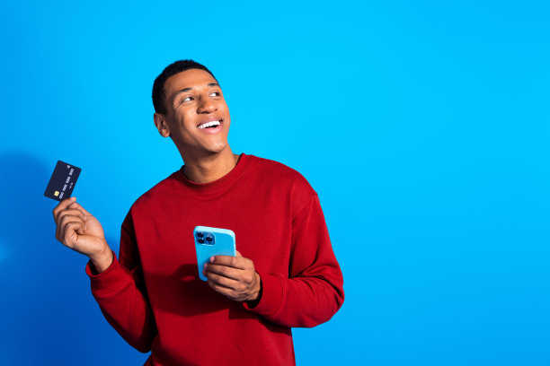 照片中，一个风趣开朗的男人穿着时髦的衣服，拿着手机，看起来很空旷，在蓝色的背景上提供无现金支付图片下载