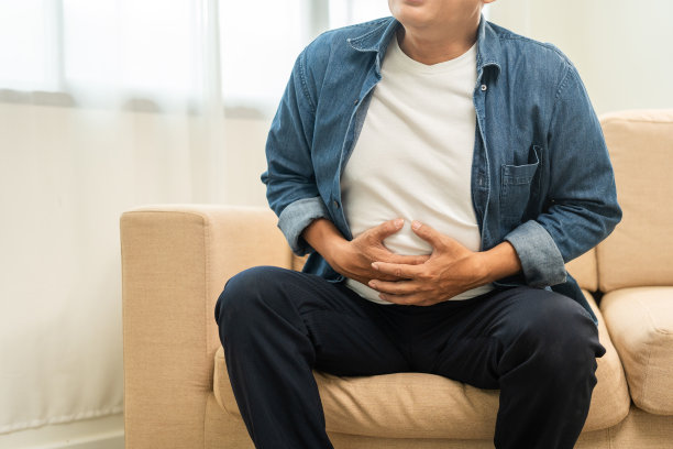 老老头有胃痛和胃炎。成熟的男人把手放在肚子上，挤一挤，放松和安抚，上厕所需要大便。坐在家里客厅的沙发上图片下载