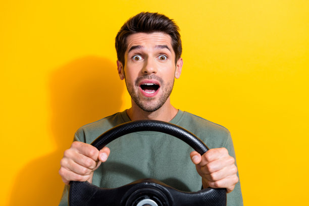 照片中，一个穿着卡其色t恤的无语男子手持方向盘，惊讶地凝视着孤立的黄色背景图片下载