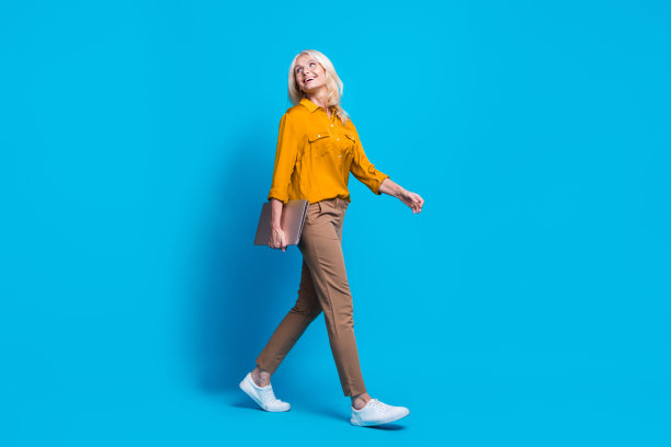 漂亮的退休女性上网本的全尺寸照片，看起来空的空间，穿时髦的黄色丝绸装孤立的蓝色背景图片下载