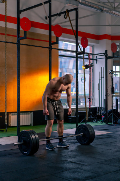 在一个体育俱乐部里，一个秃顶的教练穿着运动短裤在杠铃上举重图片下载