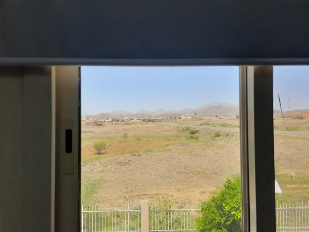 灰色的窗帘上挂着一扇窗户，外面有金属、山地沙漠、植物和建筑物的图片图片下载