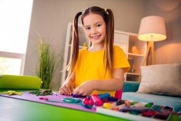 照片肖像可爱的小女孩玩橡皮泥造型穿着时髦的黄色衣服现代游戏室内部图片下载