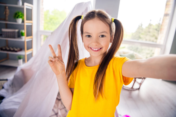 照片肖像迷人的小女孩拍自拍录像秀v字穿时髦的黄色服装儿童幼儿园游戏室图片下载