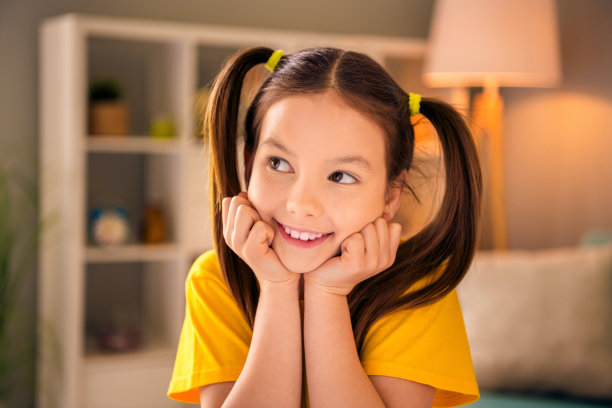 照片肖像可爱的小女孩摸拳头脸颊看着感兴趣的空间穿着时尚的黄色衣服现代游戏室内部图片下载