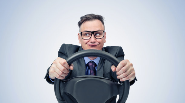 一个滑稽的商人的肖像，穿着深色西装，戴着眼镜，手里拿着汽车方向盘，背景是浅蓝色的图片下载