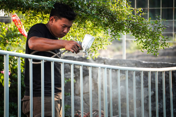 一名印尼男工人正在用高压空气喷枪粉刷栅栏。图片下载