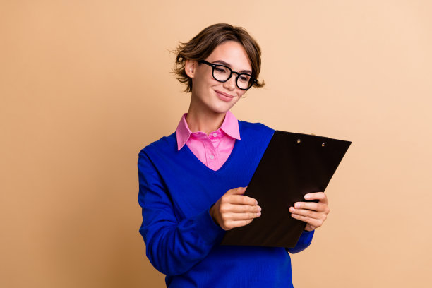 可爱的年轻女士的照片肖像拿着纸夹阅读文件合同穿着时髦的蓝色服装孤立在米色背景图片下载