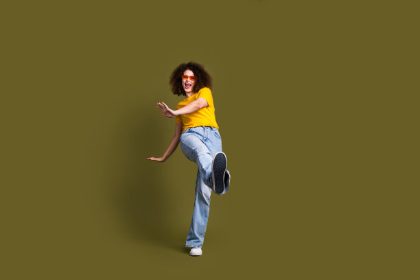 千禧一代女性的全身尺寸照片，穿着时尚的服装，走向运动鞋，鞋底品牌，在卡其色背景上孤立图片下载