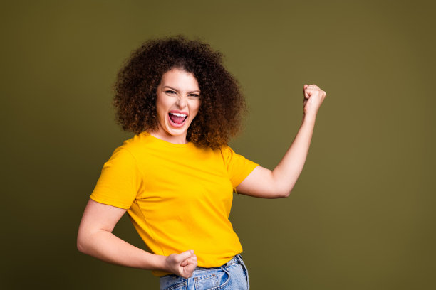 成功的照片，穿着黄色t恤的年轻女子举起拳头，在卡其色的背景上赢得胜利，并大喊着努力工作就会有回报图片下载