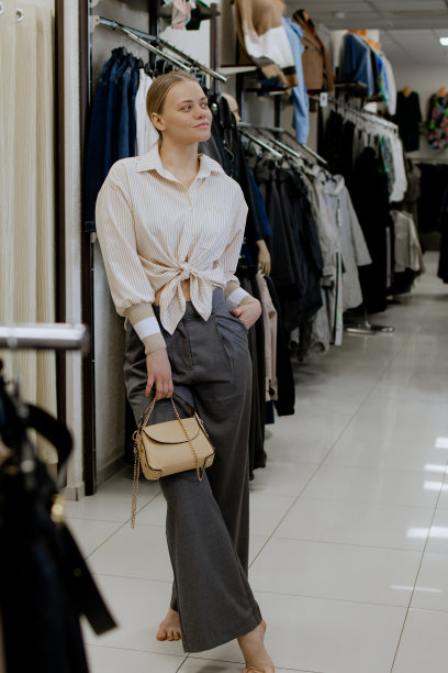 快乐的女人在更衣室里一边试穿衣服一边看着镜子里的自己，摆姿势，买休闲服装，在时尚女装店，在精品店。购物。图片下载