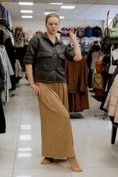 快乐的女人在更衣室里一边试穿衣服一边看着镜子里的自己，摆姿势，买休闲服装，在时尚女装店，在精品店。购物。图片下载