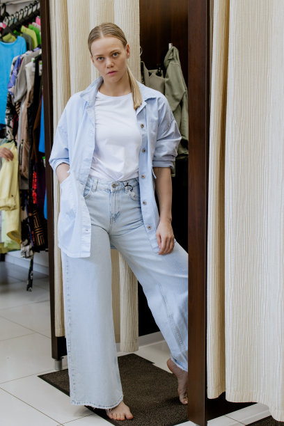 快乐的女人在更衣室里一边试穿衣服一边看着镜子里的自己，摆姿势，买休闲服装，在时尚女装店，在精品店。购物。图片下载