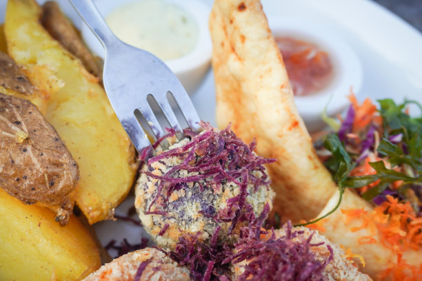 近距离照片，有人用叉子吃一盘紫色的土豆泥和油炸红薯，配上绿色的生菜和胡萝卜片图片下载