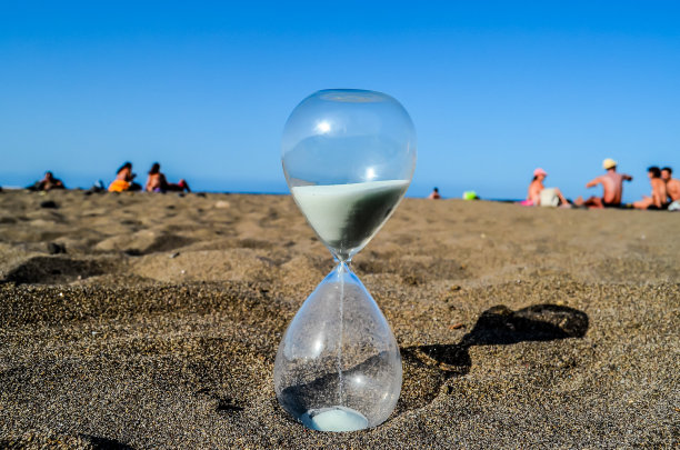 沙滩上有一个玻璃沙漏，背景是一群人图片下载