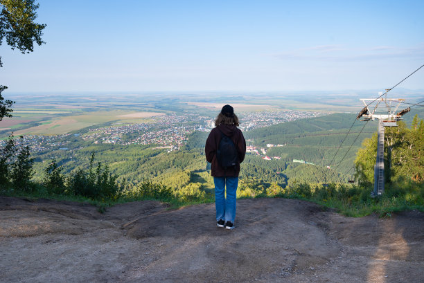年轻精力充沛的女孩背着背包，在日落时分的山崖边，在云的背景下玩耍。图片下载