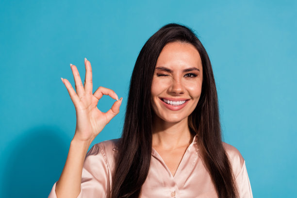 照片中，可爱的美女直发，穿着丝绸衬衫，在蓝色背景上露出可爱的眼睛图片下载