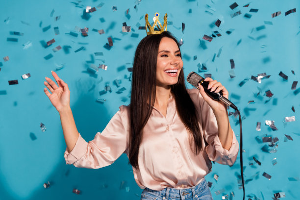 照片中的梦幻无忧无虑的女人穿着丝绸衬衫唱卡拉ok飞五彩纸屑孤立的蓝色背景图片下载