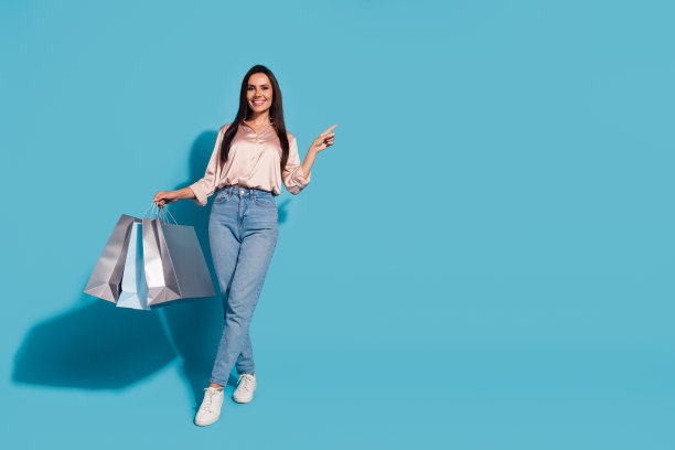 全尺寸照片的华丽可爱的女人穿着丝绸衬衫拿着购物袋表明空白空间孤立的蓝色背景图片下载