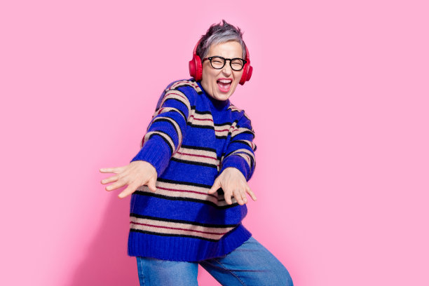 可爱的高级女士的照片肖像耳机跳舞伸展的手穿着时尚的蓝色条纹服装孤立在粉红色的背景图片下载