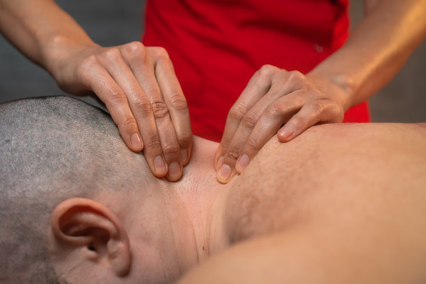 穿着红色制服的按摩师正在按摩躺在按摩台上的男子的脖子和肩膀。按摩师的手在男性脖子上的特写，按摩过程图片下载