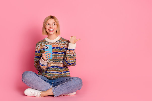 正面女性的全尺寸照片，穿着装饰套头衫，坐在智能手机上，看着粉红色背景上孤立的空白空间图片下载
