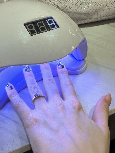 特写照片:无法辨认的女性左手展示着指甲艺术和订婚戒指，手指在指甲固化灯下展开，显示绿色格子图案的指甲油和美甲设计，在美甲沙龙的紫外线下晒指甲，高架视图图片下载