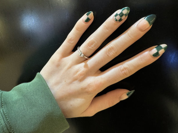 照片中无法辨认的女性左手展示订婚戒指和指甲艺术，张开的手指展示绿色格子图案指甲油美甲设计，闪亮，黑色背景，重点在前景图片下载