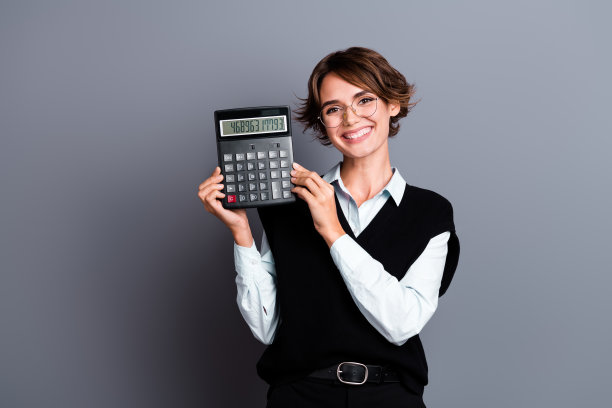 照片上的牙齿灿烂的女人戴着眼镜与鲍勃头发穿马甲衬衫演示计算器孤立的灰色背景图片下载