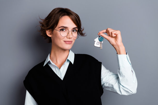 照片可爱可爱的女人穿着黑色时尚的衣服拿着钥匙广告房地产购买孤立的灰色背景图片下载