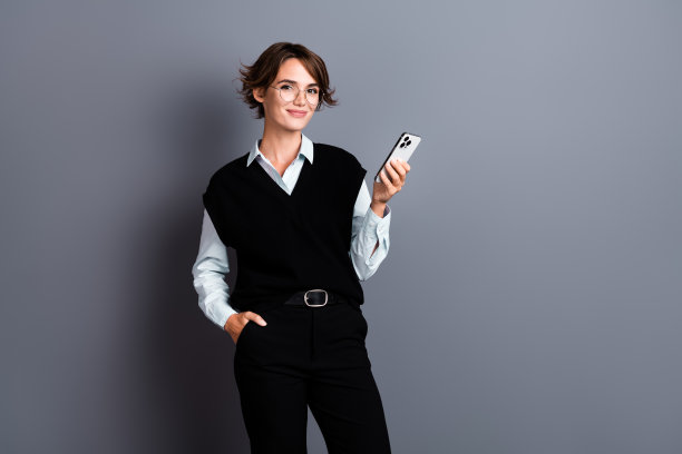 照片中，迷人可爱的美女穿着时髦的衣服，手持苹果手机，站在灰色背景的空白空间里图片下载