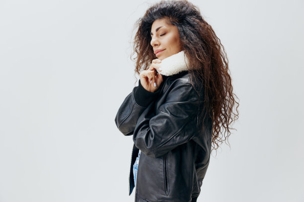 时尚卷曲漂亮的拉丁女士穿着温暖的黑色皮夹克与毛皮领闭上眼睛摆出孤立的白色工作室背景。时尚大甩卖新系列概念简介图片下载