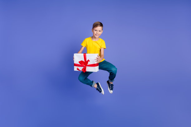 照片正面高兴可爱的男孩穿着时尚的黄色衣服庆祝节日收到大礼物孤立在紫色的背景图片下载