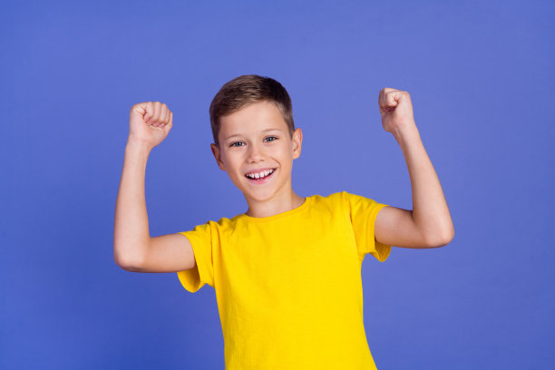 照片的快乐积极的好男孩穿着时尚的黄色衣服举手拳头耶孤立在紫色的背景图片下载