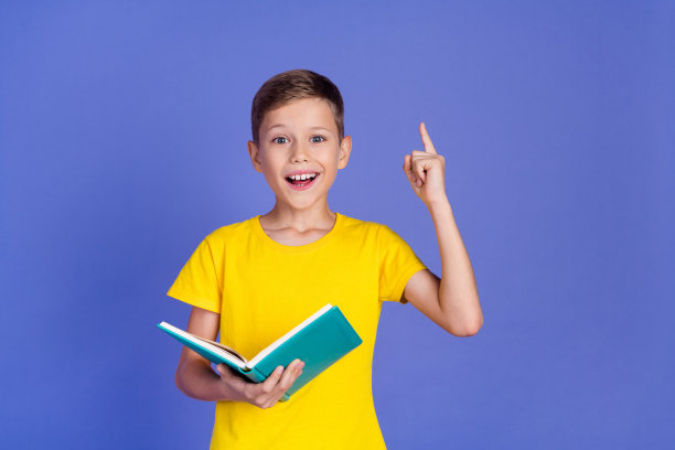 照片中，兴奋的疯狂男孩穿着时尚的黄色衣服读科幻小说，手指向上孤立在紫色的背景上图片下载