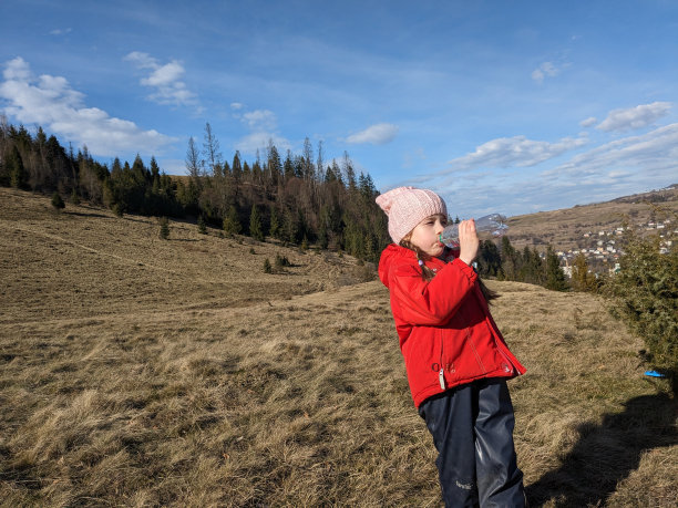 一个女孩在山坡上用塑料瓶喝水。照片。图片下载